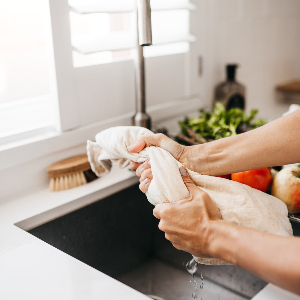 
                      
                        The Swag reusable produce bag for the fridge with a natural trim being wrung out after being dampened down under the tap  - The Swag AU
                      
                    