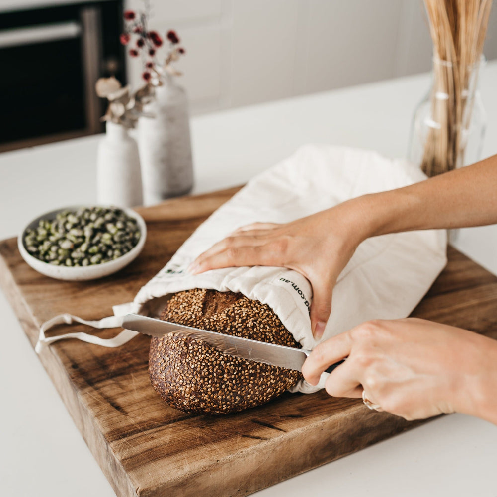 
                      
                        The reusable bread bag on a wooden bread board with sourdough bread being cut up - The Swag AU
                      
                    