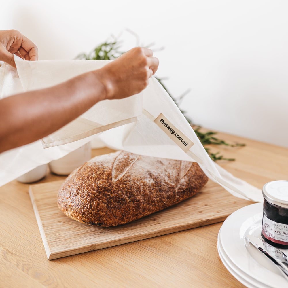
                      
                        The 100% natural and reusable food cover, covering a loaf of bread on a wooden copping board - The Swag AU
                      
                    