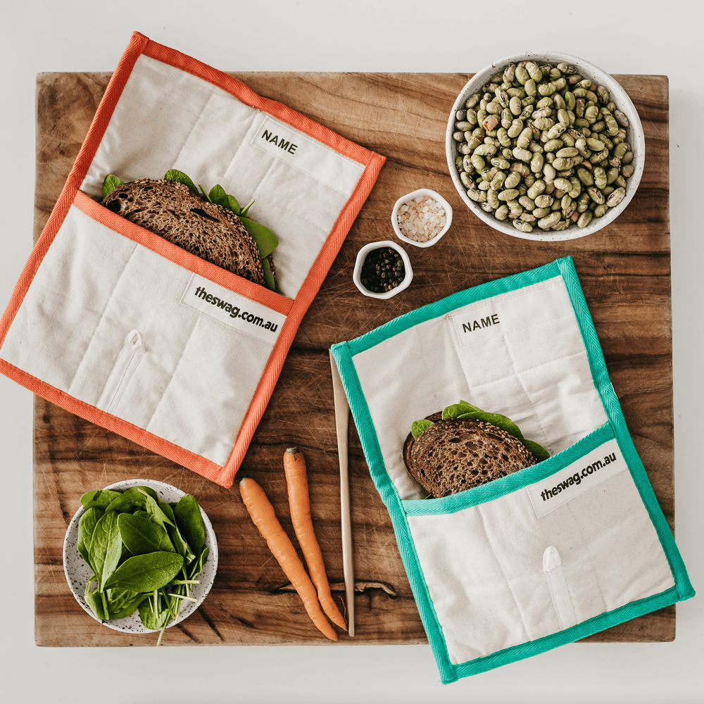 
                      
                        The Swag orange and one green reusable Lunch Swag opened up on a wooden chopping board and containing sandwiches - The Swag AU
                      
                    