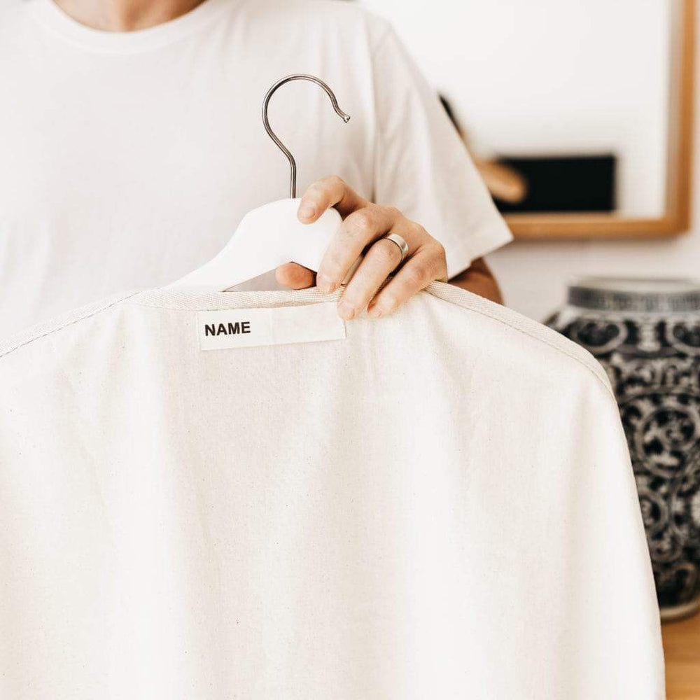 
                      
                        The Swag  - a woman holding The reusable Clothes Swag while showing the name tag section on the back of the Clothes Swag - The Swag AU
                      
                    